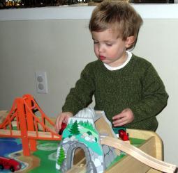 A young boy wearing a green shirt plays with a train set.