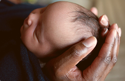 An infant's head is cupped in the hands of its caregiver.