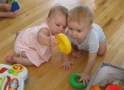 Two babies sit on the floor, playing with colorful plastic rings.